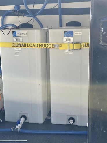 Two large containers labeled Fresh Water and Sanitizer secured with a yellow strap.