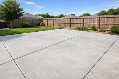 Clean concrete patio in a fenced backyard with green lawn and shrubs.