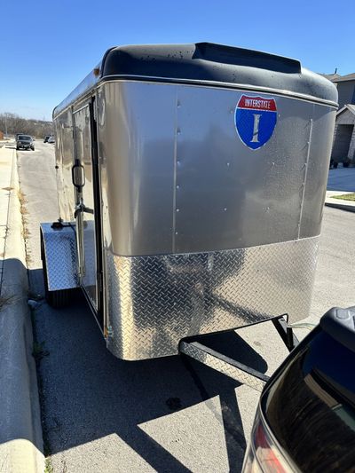 Silver enclosed trailer parked on the street under clear blue sky.