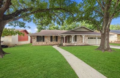 Single-story stone house with large trees and green lawn.