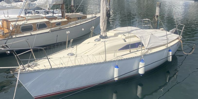 White sailboat docked with blue and white fenders in calm water.