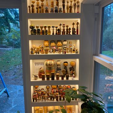 Shelves filled with illuminated traditional wooden kokeshi dolls in a cozy room corner.
