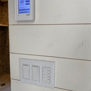 Digital thermostat and light switches on a white paneled wall.