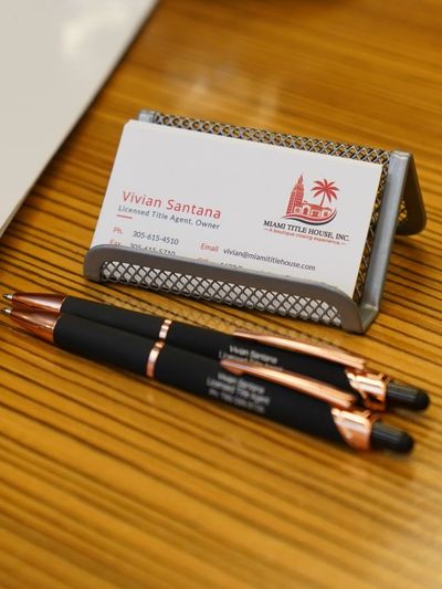 Business card of Vivian Santana with pens on a wooden desk.
