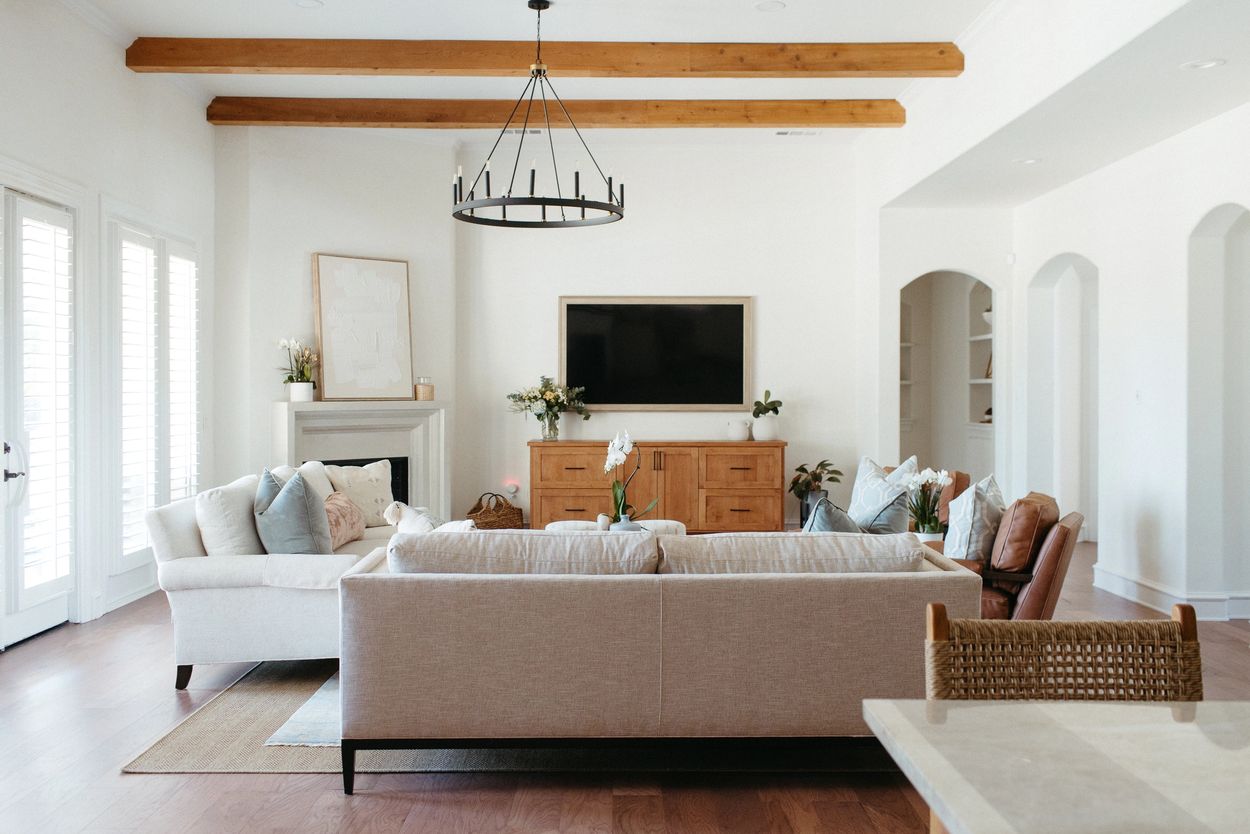 Southlake living room with exposed wood ceiling beams, white sofas, arched openings, and warm wood accents.