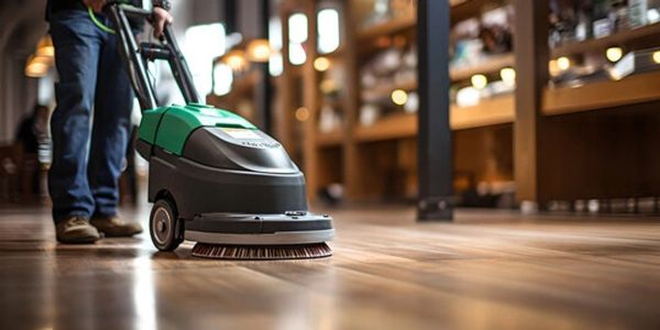 Person using a floor cleaning machine on a wooden surface indoors.