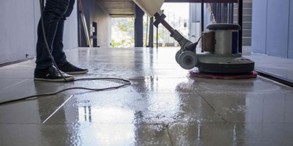Person cleaning floor tiles with a floor polishing machine.
