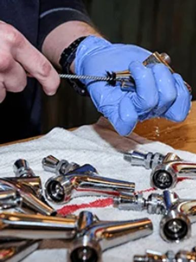 Person cleaning metal nozzles with a brush while wearing a blue glove.