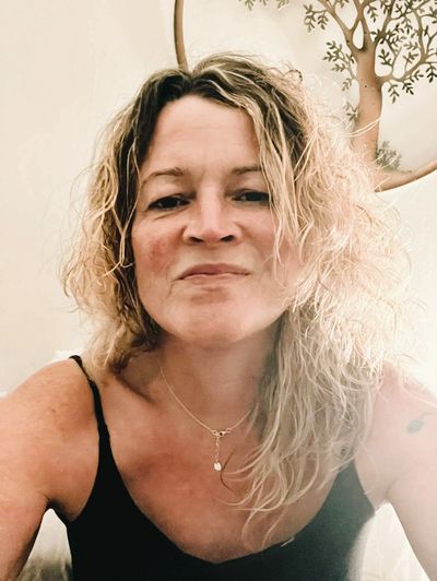 Woman with curly blonde hair wearing a black top and a necklace.