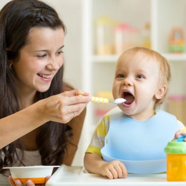 A mother happily feeding her baby with a spoon.