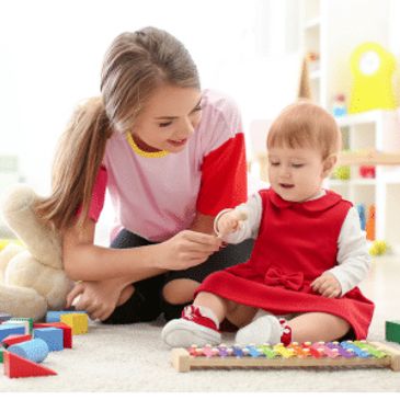 A woman playing with a baby surrounded by toys indoors.