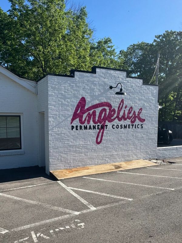 White building with 'Angelise Permanent Cosmetics' painted on the wall in pink and black.