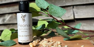Feonix Naturals Face &amp; Hand Oil bottle with natural resin pieces and green leaves.