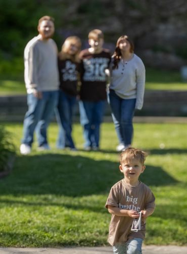 A young boy walks in front of a blurred family in a park.