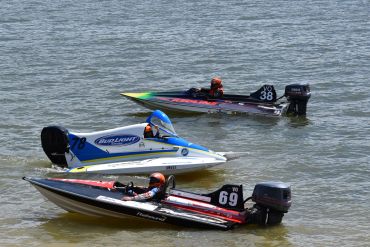 Three motorboats racing on the water near the shore.