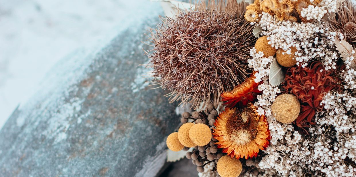 A dried native bouquet in tones of rust, orange and yellow rests against a small dolerite boulder on