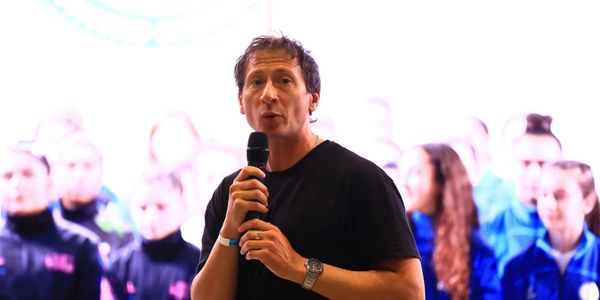 Man speaking into microphone in front of blurred audience.