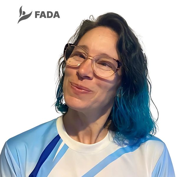 Woman with blue-dyed hair and glasses smiling, wearing a sports shirt with FADA logo.