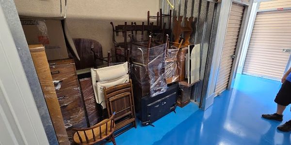 A storage unit filled with wrapped furniture and a person standing inside.