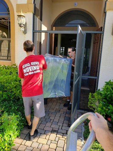 Two movers carrying a large wrapped item through a doorway.