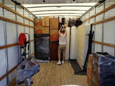 Person organizing packed furniture and boxes inside a moving truck.
