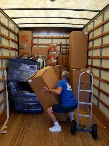 A man lifting a large box inside a moving truck filled with packed items.