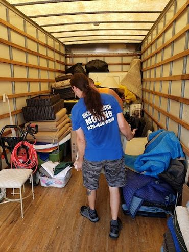 Mover organizing furniture and blankets inside a moving truck.