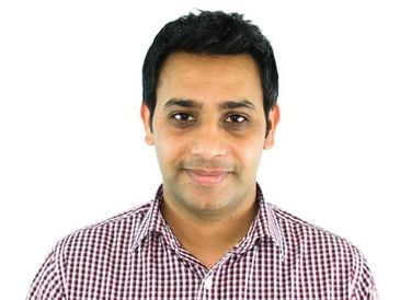 Portrait of a smiling man in a checkered shirt against a white background.