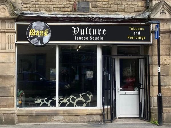 Front view of Vulture Tattoo Studio with a black and white cow-patterned bench inside.