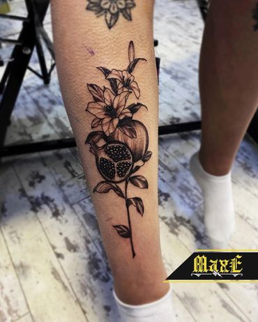 Black ink tattoo of a pomegranate and flowers on a leg.