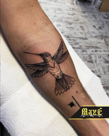 Realistic hummingbird tattoo on forearm with detailed shading and wings spread.