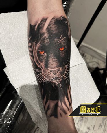 Realistic black panther tattoo with striking orange eyes on forearm.