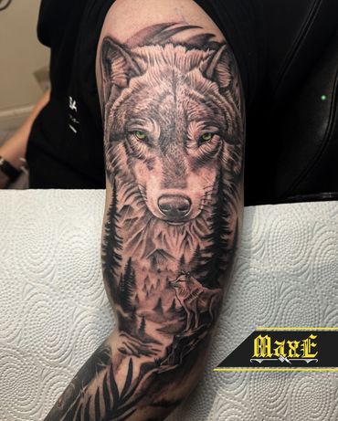 Realistic wolf tattoo with forest and smaller wolf on forearm.