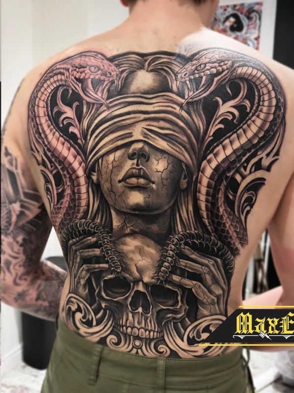Intricate back tattoo of a blindfolded woman, two cobras, and a skull with horns.