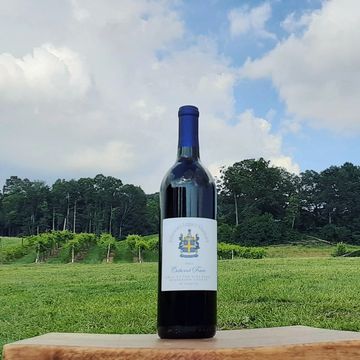 A wine bottle on a wooden surface with a vineyard and blue sky background.