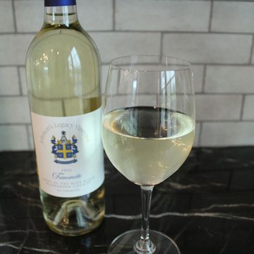 A bottle and glass of white wine on a dark marble surface.