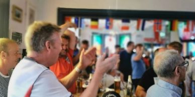 Group of men clapping and enjoying drinks in a lively pub.