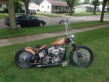 Custom motorcycle with a brown fuel tank and high handlebars parked on grass.