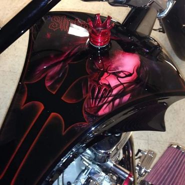 Custom motorcycle gas tank with a red skull design and crown cap.