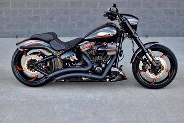 Sleek black motorcycle with orange accents parked against a gray brick wall.