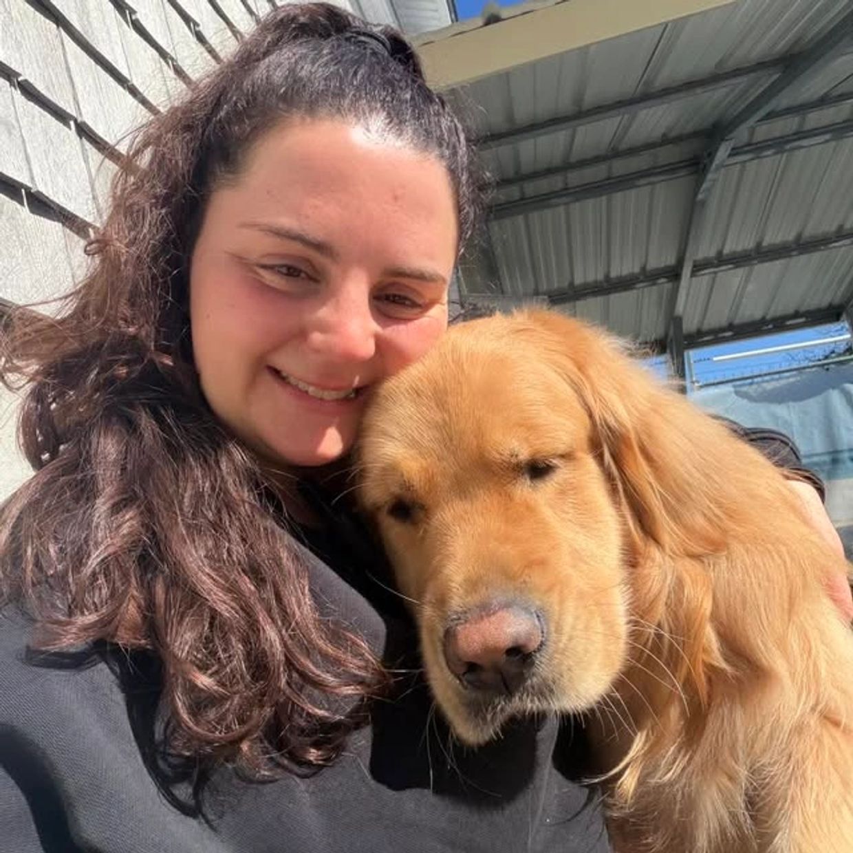 Woman smiling and cuddling a golden retriever dog outdoors.