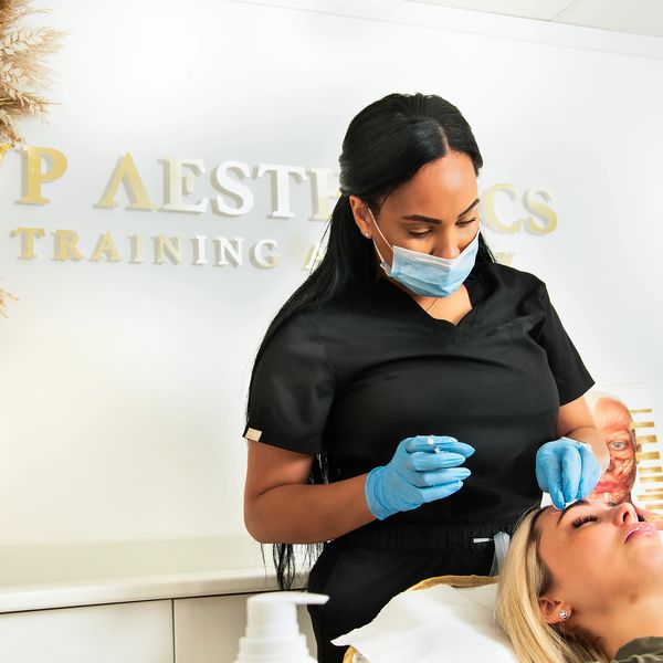 Aesthetician wearing mask and gloves treating a client's face in a clinic.