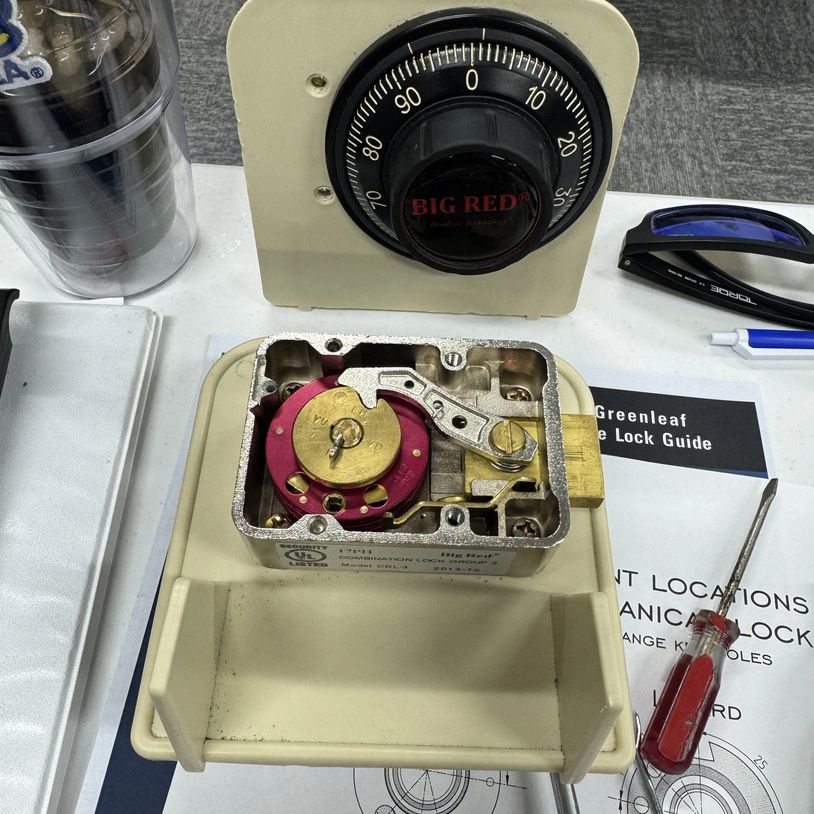 Disassembled combination lock with tools and guide on a workbench.