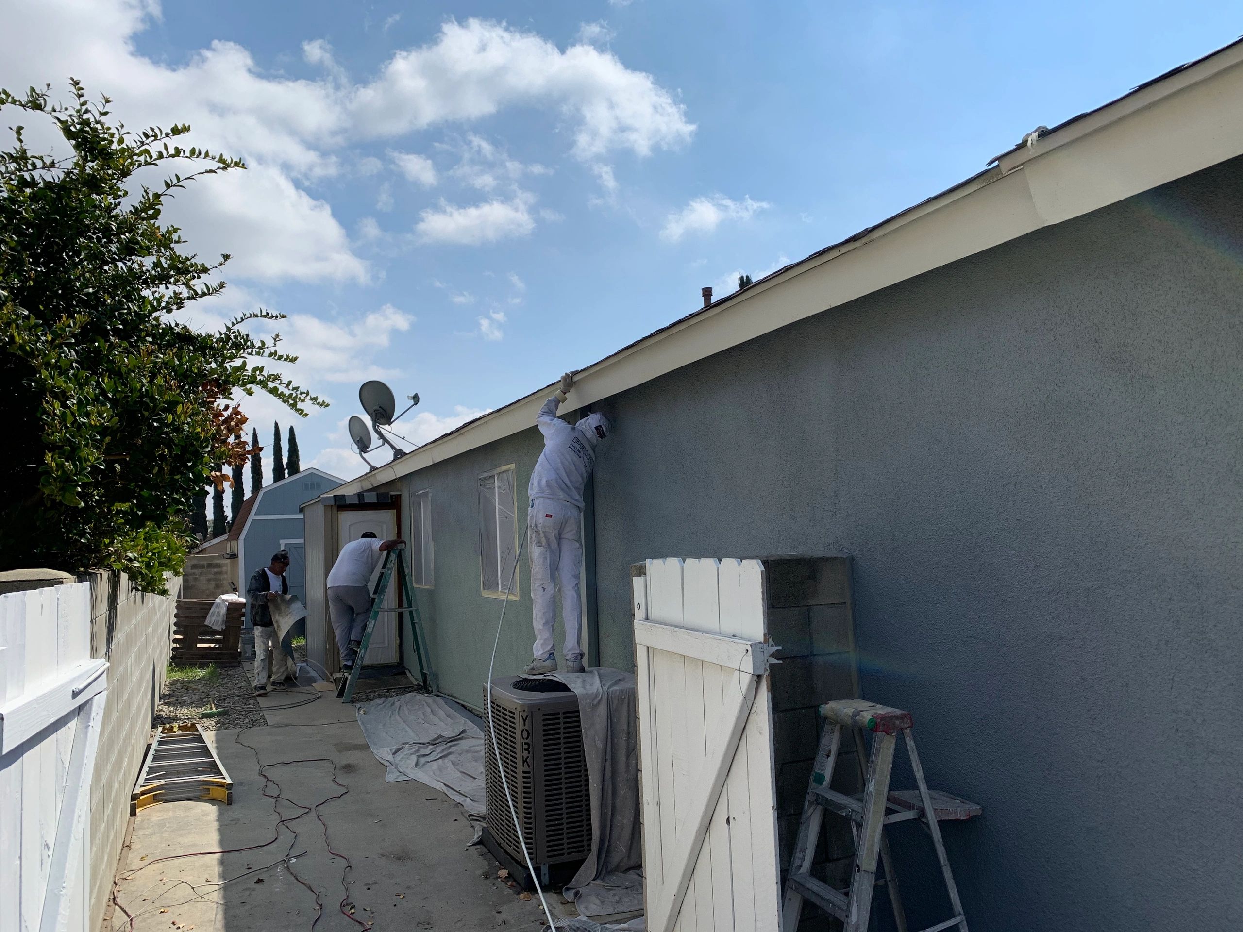 Painters working on a house exterior on a sunny day.