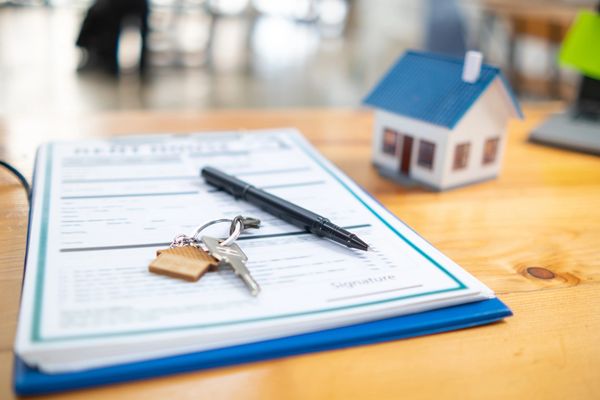 A close-up of a house model, keys, and a pen on a contract, symbolizing real estate transaction
