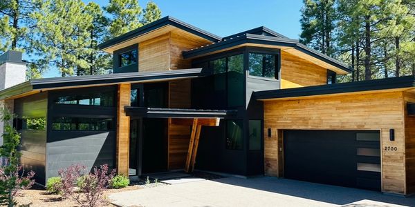 Modern two-story house with wood and black exterior under clear blue sky.