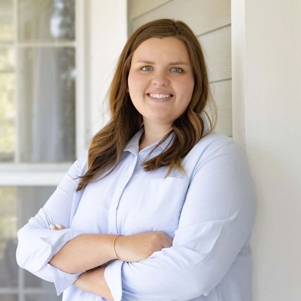 Woman with folded arms smiling against a light-colored wall.