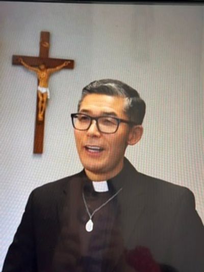 A priest standing with a crucifix in the background.