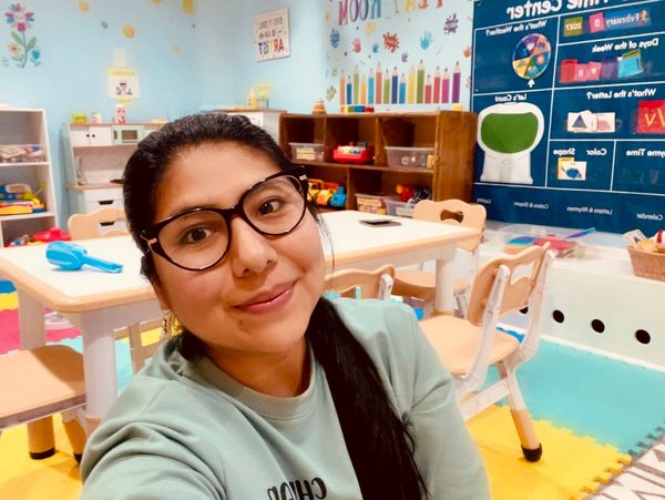 A preschool teacher smiling in a brightly decorated, organized classroom