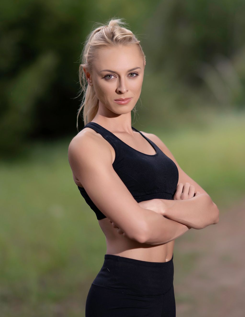 Confident woman in black athletic wear with arms crossed outdoors.